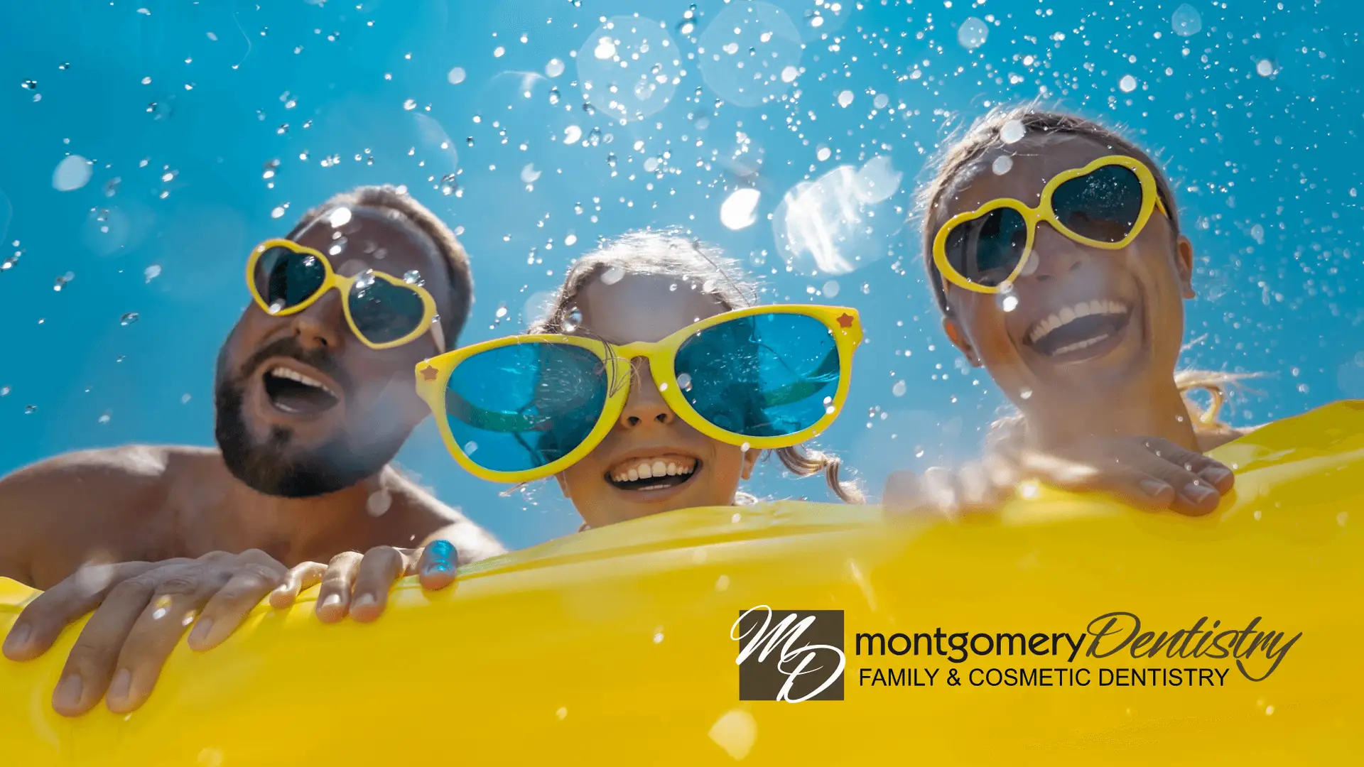 A family of three smiling on a water float with big sunglasses on in the sun