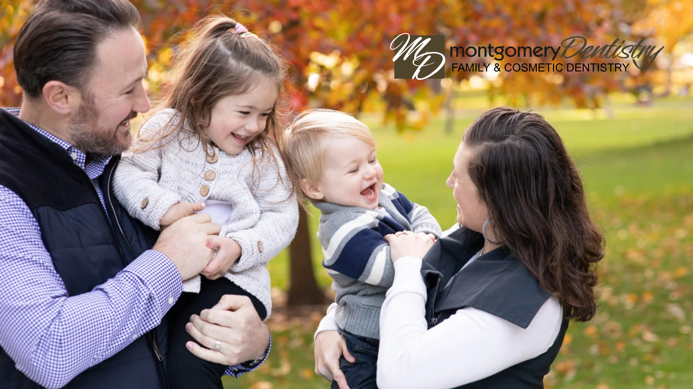 Happy family of four smiling in grass during fall dental care tips