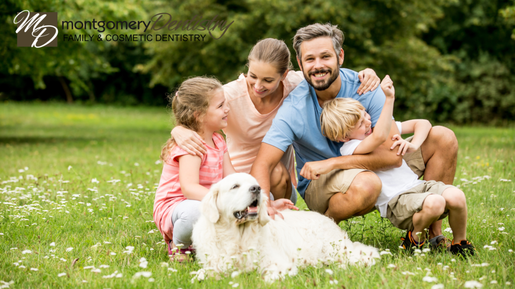 Smiling family of four and dog in green field. Montgomery Dentistry logo in top left corner.