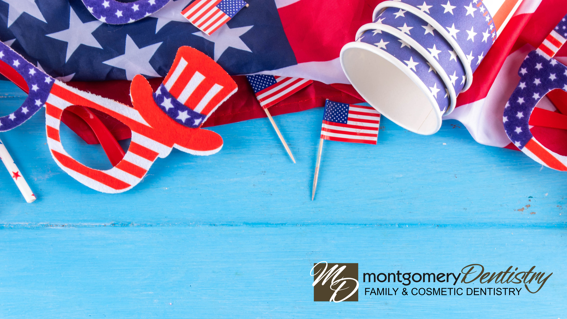 Fourth of July party hats, cups, and flags laid on a blue table. Montgomery Dentistry logo at bottom right.