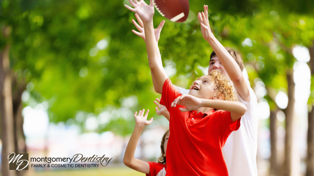 Kids playing football with green foliage in the background. Montgomery Dentistry logo in the bottom left corner.